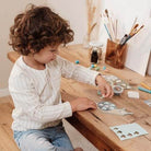 Child engaged in creative crafting with stickers and materials at a wooden table, showcasing imagination and fun.