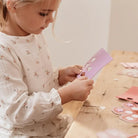 Young girl crafting with colorful paper in a creative workspace, engaged in imaginative play.