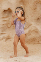 Little Dutch mauve swimsuit with straps modeled by girl in sandy outdoor setting