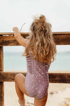 Girl wearing mauve sleeveless swimsuit by Little Dutch, playing by the beach.