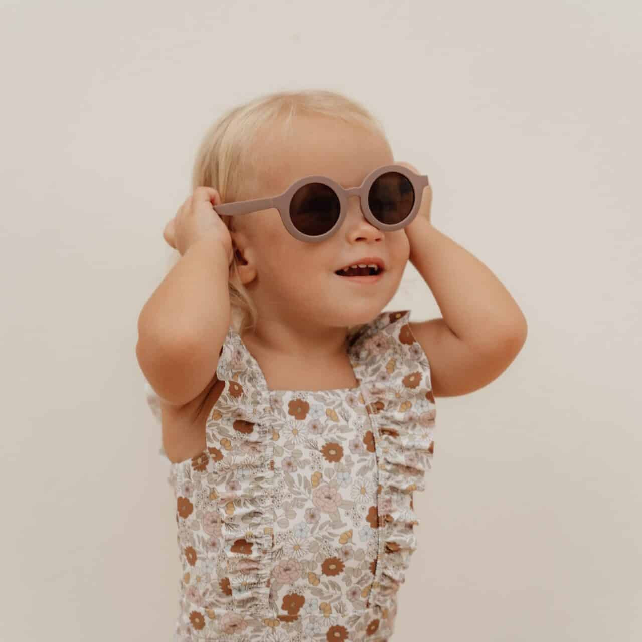 Girl wearing Fato de Banho Folhos - Vintage Little Flowers swimsuit by Little Dutch, smiling with sunglasses on.