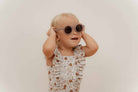 Girl wearing Fato de Banho Folhos - Vintage Little Flowers swimsuit by Little Dutch, smiling with sunglasses on.