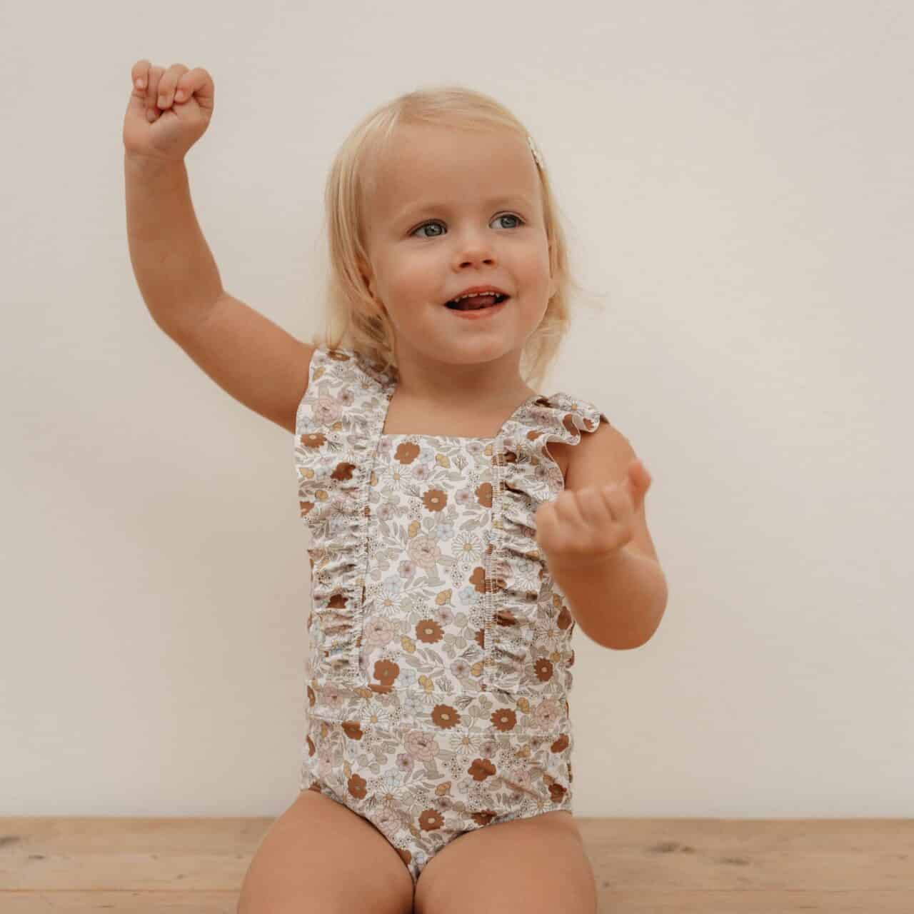 Toddler wearing Little Dutch Vintage Little Flowers ruffled swimsuit, enjoying in a playful pose against a neutral background