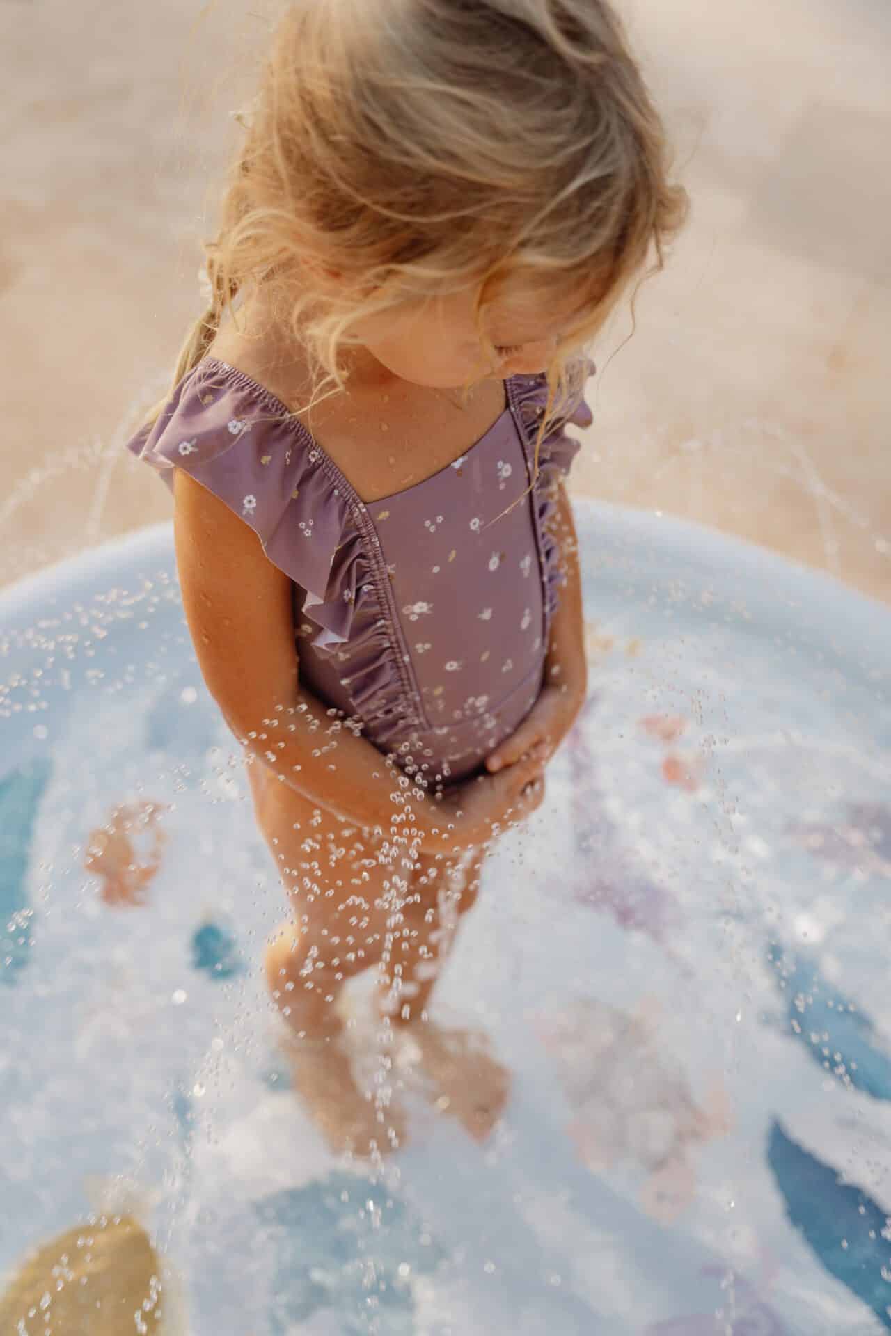Little girl wearing a mauve Little Dutch sleeveless swimsuit playing in a splash pool