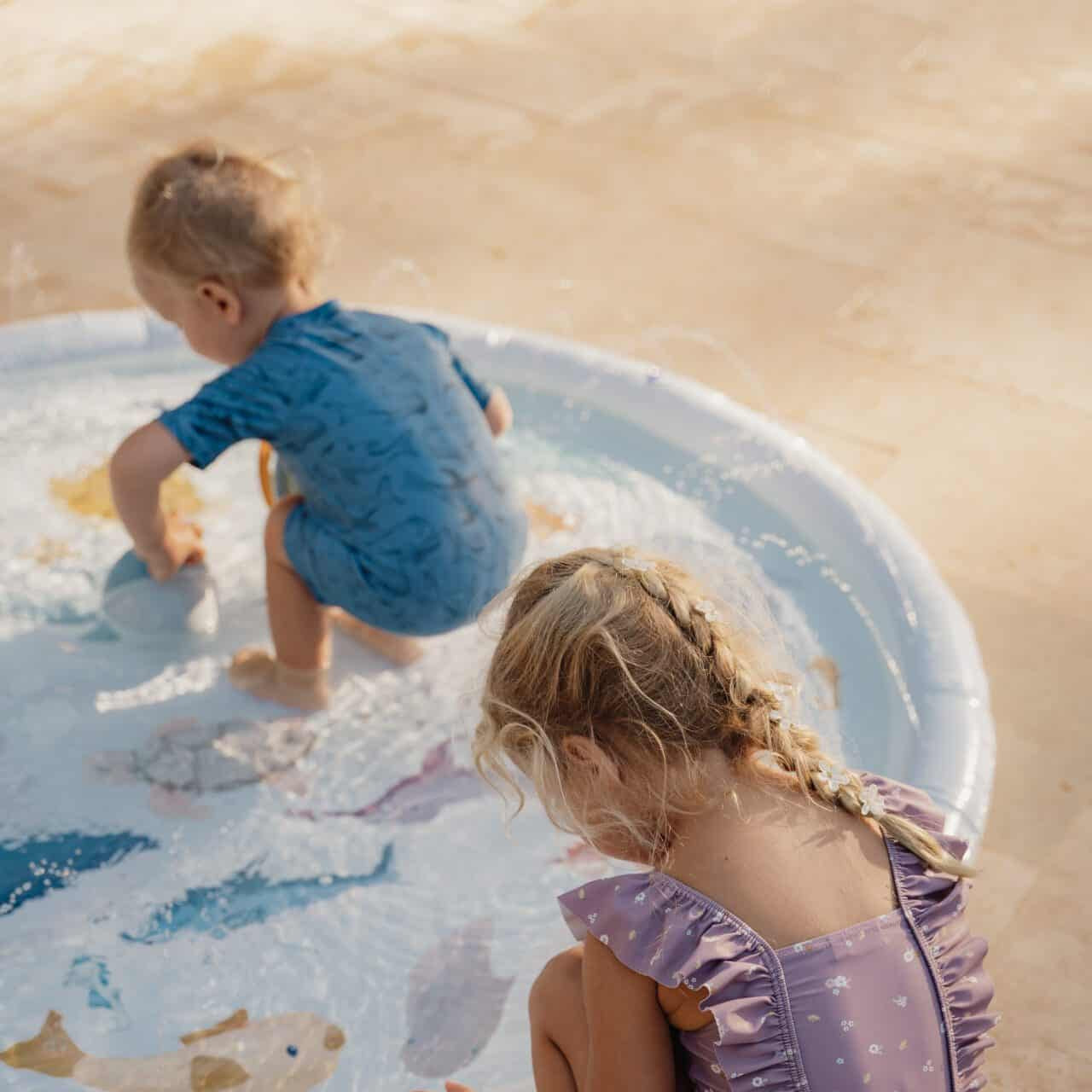 Girl wearing mauve Little Dutch swimsuit playing in a kiddie pool with another child.