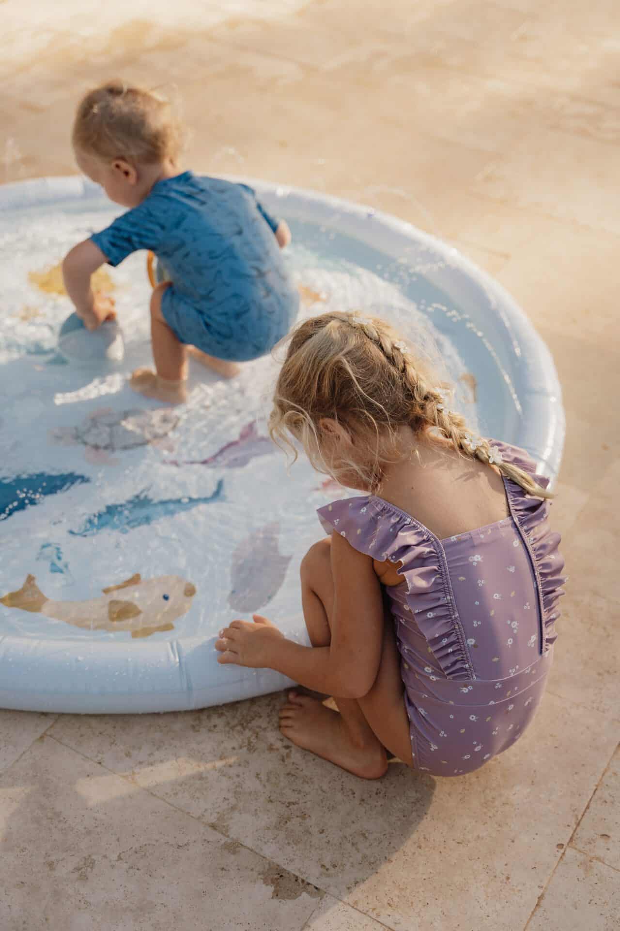 Girl wearing mauve Little Dutch swimsuit playing in a kiddie pool with another child.