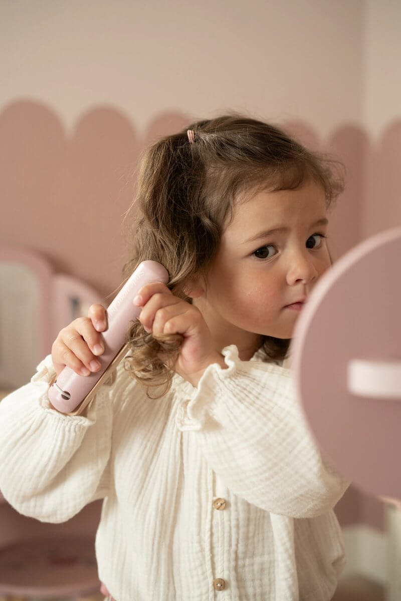 Criança usando o Conjunto de Cabeleireiro Little Dutch com uma prancha de alisar em um salão de beleza imaginário.