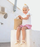 Criança sorridente usando sandálias Igor tamanho 23, segurando uma cesta de palha, em um ambiente de verão.