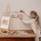 Girl using finger painting set, displaying colorful artwork inspired by nature on a wooden easel.