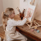 Girl painting at easel with vibrant colors, exploring creativity with the Little Dutch Fairy Garden art set.