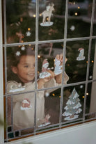 Child placing colorful Christmas stickers on a window, creating a festive holiday scene.