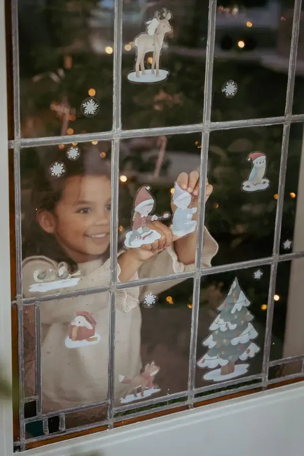 Child decorating window with festive Christmas stickers from Little Dutch, creating a joyful holiday scene.