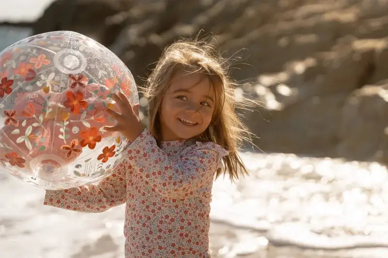Girl playing with a 3D inflatable beach ball featuring pink flowers by the shore.