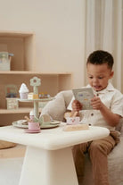 Criança brincando com a Bandeja de Bolos Little Dutch, organizando chá com doces e menu ilustrado.