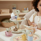 Bandeja de Bolos Little Dutch com andares decorada com doces e acompanhada por criança em ambiente de chá.