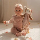 Baby sitting on a soft surface holding a Doudou corça Fairy Garden toy by Little Dutch, radiating joy and comfort.