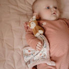 Baby lying on a soft blanket, holding a Doudou macio Corça from the Fairy Garden collection by Little Dutch.