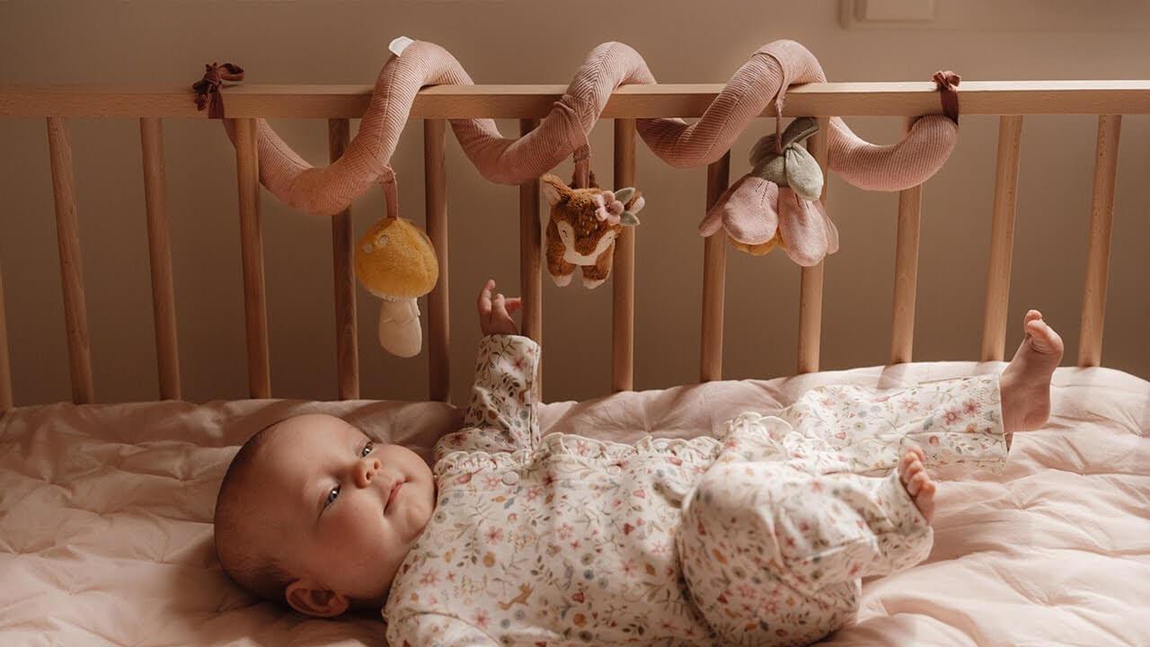 Baby playing under the Little Dutch Fairy Garden activity spiral in a cozy crib setting.