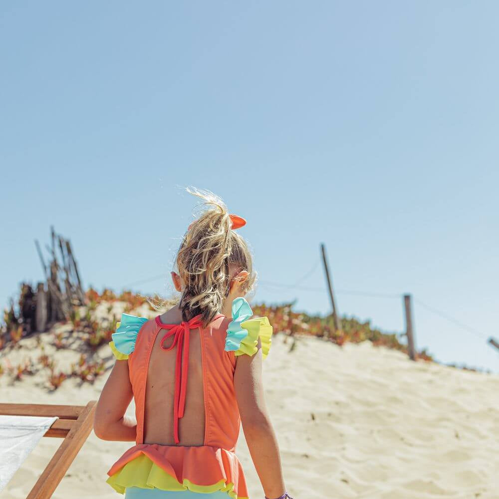 Menina usando fato de banho Candy Colors da Paper Boat na praia, destacando design colorido e confortável.
