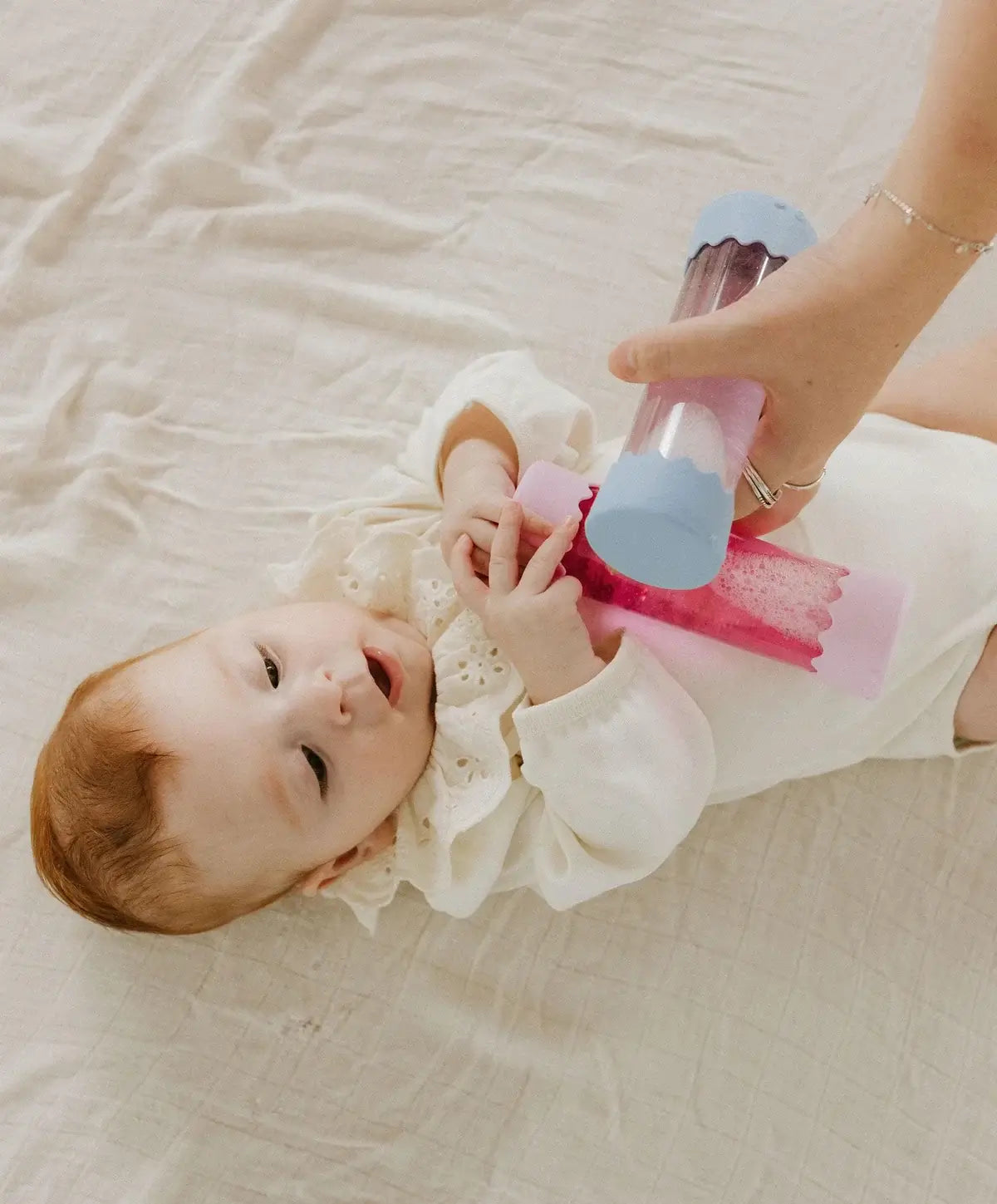 Bebé brincando com a Garrafa da Calma Bebé - Pink da Jellystone em uma superfície suave.