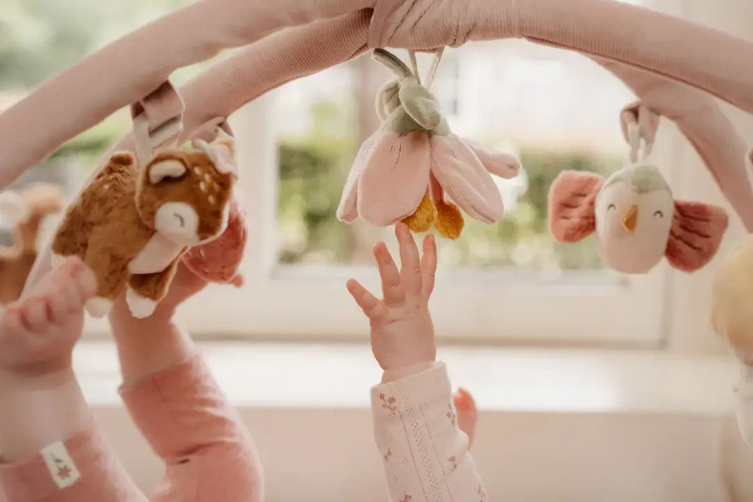 Bebé alcançando brinquedos de pelúcia pendurados em arcos do Ginásio e Tapete de Actividades Fairy Garden.