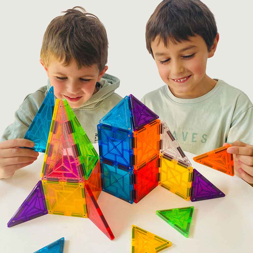 Two boys joyfully building a colorful structure with geometric magnetic tiles, showcasing creativity and play.