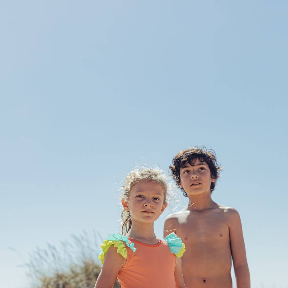 Menina e menino na praia com fato de banho de Candy Colors da Paper Boat, destacando design vibrante e colorido para o verão.