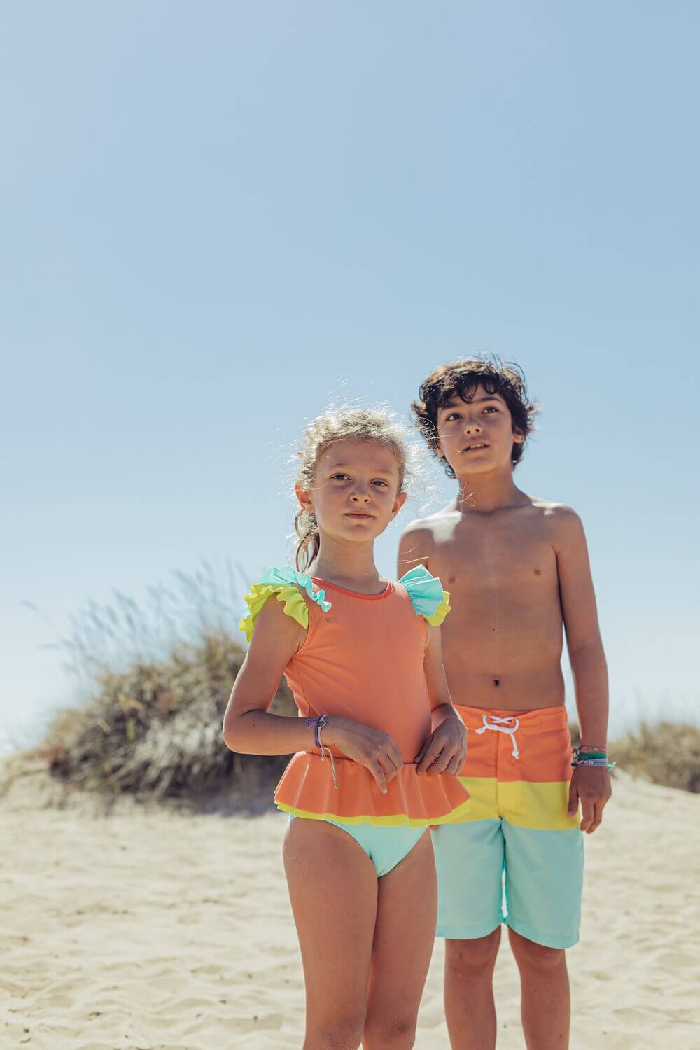 Menina e menino na praia com fato de banho de Candy Colors da Paper Boat, destacando design vibrante e colorido para o verão.