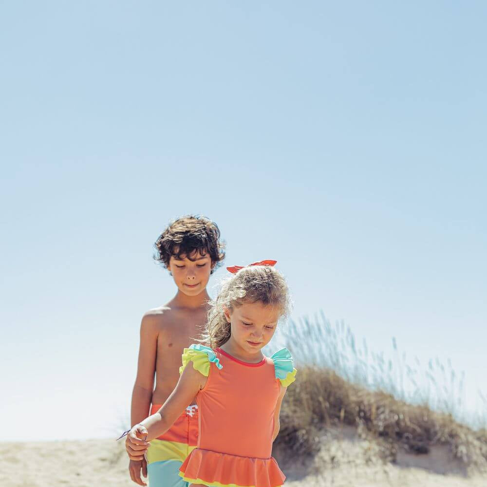Two children playing on the beach, girl in Paper Boat's Candy Colors swimsuit designed in Portugal with high-quality materials